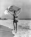 Fun loving Ann Miller, here captured while running on a Malibu Beach by Ned Scott, goes the extra mile to support her role for the Columbia Studios film, Eadie Was A Lady, 1945. Ann plays the role of Edi Alden, a nightclub dancer who is supporting herself while attending college courses. Director Arthur Dreifus’ musical comedy, Eadie Was A Lady, 1945. Notice the tandem surfing design on Ann’s towel which billows in the wind above her head. This scene is the beach below the cliffside residence of sculptress Cornelia Runyon.