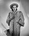 Columbia Studios dancer Ann Miller poses for this fashion photograph in a full length leopard coat with turned back cuffs. The coat is an original design by Willard George of Los Angeles. The hat is an off-the-brow beret by John-Fredericks.
