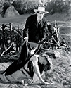 Movie Stagecoach: The caption pasted to the back of this 1939 print reads: "With pity, Hatfield (John Carradine), the cold blooded gambler in "Stagecoach", places a cloak over the doughter of the relay station keeper who has been murdered by Apaches. The ocoach, with its nine passengers has just arrived only to find the staion burned and everyone dead. The delay enables the Indians to prepare for an attack on the stage in Walter Wanger's presentation of pioneer days. 