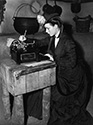 Louise Platt in costume on the set of Stagecoach takes a moment to type a letter between scenes