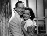 An on-set scene with Joan Bennett and Fredric March. The studio caption with this photograph reads: Sam (Fredric March) and Kay (Joan Bennett) come at last to a perfect understanding." After a long voyage west over the Pacific ocean from San Francisco, detective Sam Wye, the vigorous pursuer, and Kay Karrigan, the accused murderer, reconcile in a hotel room in Singapore. Director Tay Garnett's easy going detective mystery, "Trade Winds", 1938.