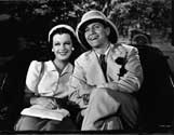 An on-set scene with Joan Bennett and Fredric March. The studio caption with this photograph reads: "Sam, (Fredric March) and Kay (Joan Bennett) having become good friends, enjoy a jinrikisha ride through the outskirts of Singapore." Such chumminess between these two was not in the plan as Sam, private detective, began chasing Kay, accused murderer, in San Francisco, but she slipped through his fingers by boarding an outward bound vessel for the Orient. Director Tay Garnett's lighthearted detective mystery, "Trade Winds", 1938.