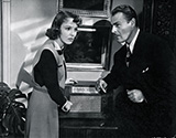 A tense moment as two characters from Fritz Lang's 'Hangmen Also Die' listen for any news broadcast about the assassination of Reich Protector Reinhold Heidrich and the resulting actions taken by occupying Nazi forces. Actors Anna Lee and Brian Donlevy play Masha Novotny and Dr. Svoboda, both key role players in the ensuing action as the plot of this suspenseful WWII drama unfolds.
