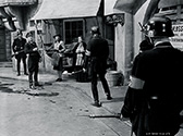 Nazi Gestapo troops scour the streets of Prague hunting for the assassin of Reich Protector Reinhard Heidrich. Anna Lee as Masha Novotny and market proprietor Margaret Burt are transfixed with fear when Lane Bradford as the Gestapo officer directs troops in search efforts. Fritz Lang's Hangmen Also Die, 1943