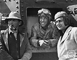 A rare off-set photograph of key personnel for a war film from Columbia Pictures in 1943. Director Zoltan Korda with ever-present tobacco pipe poses to the left of the film's male star, Humphrey Bogart while to the right of center stands the film's producer, Sydney Buchman. This war film was shot on location around the sand dunes near Yuma, Arizona.