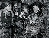 Sharing a cigarette with his Army buddies, Burgess Meredith as Ernie Pyle underscores the fact that he shared the privations of his regular soldiers while they were hunkering down in an improvised shelter, safe from enemy action, during inclement weather.