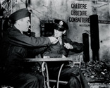 Lee Miller extends a courtesy to Ernie Pyle, lighting his cigarrette while both men take a monent's pause while on the movie set of Story of G.I. Joe. Dressed in their War Correspondent's uniforms, both men assisted in the making of the film by polishing the script. And the presence of Ernie Pyle energized the combat war veterans who participated in the film as cast members. Both men were very good friends having been in the news business together for many years. There is an ease, an intimacy shown here between these two which only the ritual of lighting a cigarrette can properly convey.