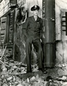 Ernie Pyle takes a break on the bombed out set of the movie Story of G. I. Joe. Leaning against metal stack, Ernie sizes up the situation while dressed in his War Correspondent's uniform.