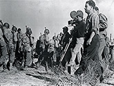 Director William Wellman, at left of camera, directs a rehearsal of a scene for Ernie Pyle's "Story of G.I. Joe" involving actual "GI's" whom the U.S. Army lent for important battle scenes in Lester Cowan's production. Second assitant director, Jimmy Petch, stands in the foreground with a very determined expression. Director William Wellman's authentic wartime drama, "The Story of G.I. Joe", 1945.