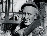 After a successful forward surge by the company at the front, Burgess Meredith as Ernie Pyle takes a moment to relax in the shelled remains of a building in a small Italian town. Meredith is actually sitting in the back seat of a car, the only part of the car still remaining after the attack. Scene from The Story of G.I. Joe. 