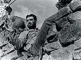 An Army private, combat veteran with the 34th Infantry Division, relaxes in the crotch of a shelled masonry wall with a cigar after a successful attack at the front. Scene from The Story of G.I. Joe.