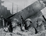 Pvt. Billy Benedict as himself, Captain Walker (Robert Mitchum) and Ernie Pyle (Burgess Meredith) crowd into a protective position, with Thompson machine guns at the ready, while they surveil the enemy activities a short distance away.