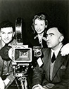 Cinematographer Russel Metty on the left, poses with associate producer David Hall and composer Ann Ronell as they flank the 35mm camera. 
